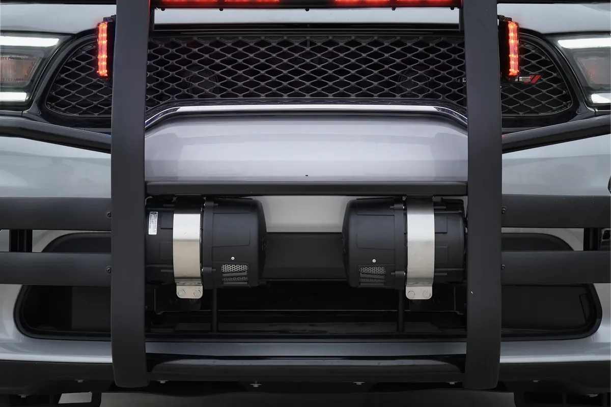 Two Feniex Hammer low-frequency sirens mounted under the front bumper of a silver SUV, behind a push bumper with red warning lights