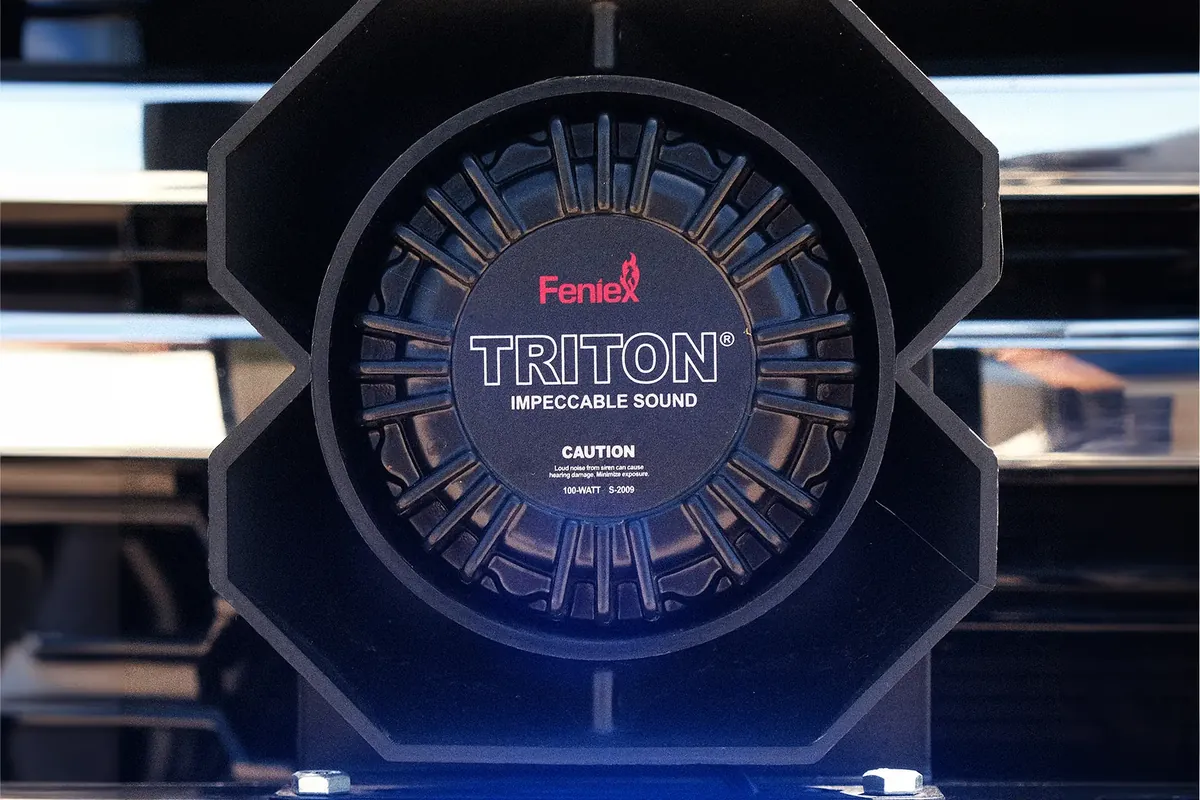 Feniex Triton 100-watt siren speaker mounted in front of a vehicle's chrome grille