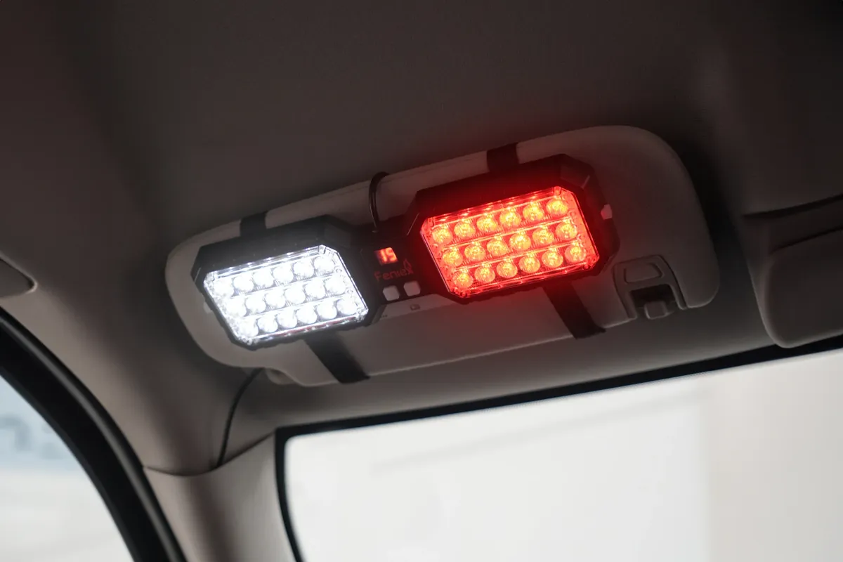 Feniex Interior Visor Light strapped to a car's sun visor, one head lit white and one lit red
