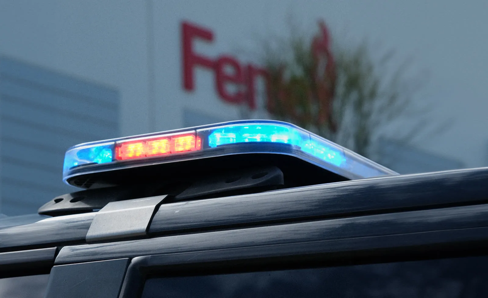 Feniex lightbar lit blue, red and white on the roof of a black vehicle outside the Feniex building