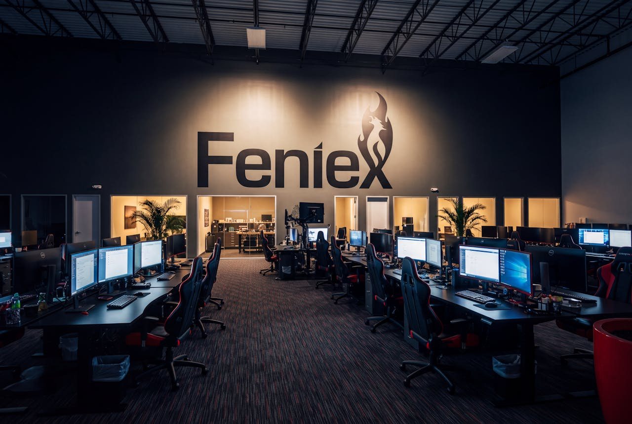 The Feniex open-plan office after hours, every monitor awake and the Feniex wordmark lit on the far wall.